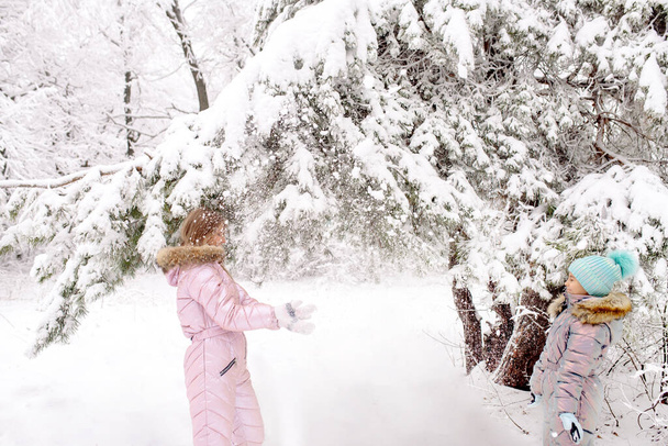 Mom and daughter in warm winter overalls for a walk in the winter forest: active games, playing snowballs and other activities - Foto, Imagen