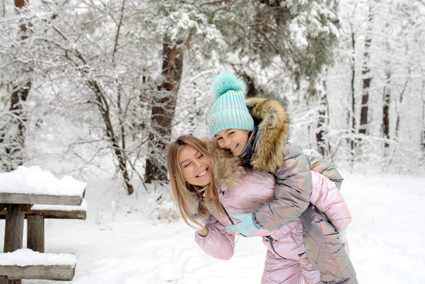 Mom and daughter in warm winter overalls for a walk in the winter forest: active games, playing snowballs and other activities - Фото, изображение