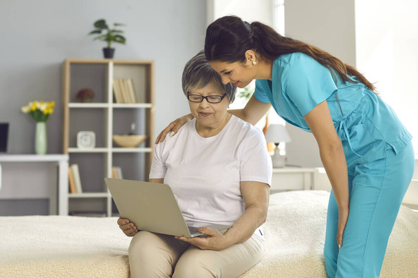 Woman nurse helping elderly lady patient with laptop at home lifestyle portrait - Foto, Bild