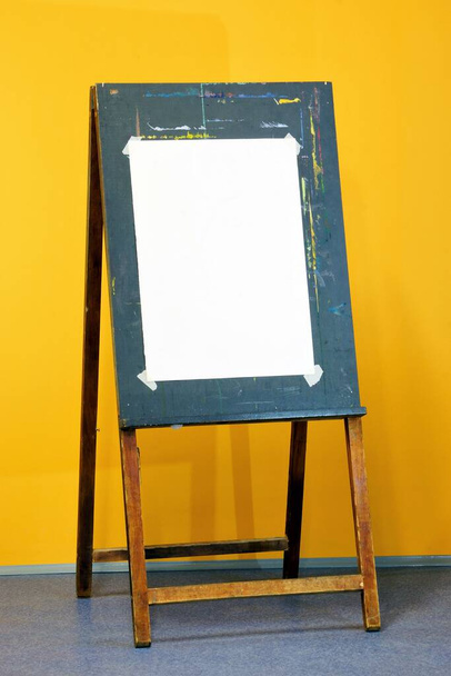 An easel and a sheet of drawing paper. A wooden stand on which the artist places a painting or drawing while working. - Photo, Image