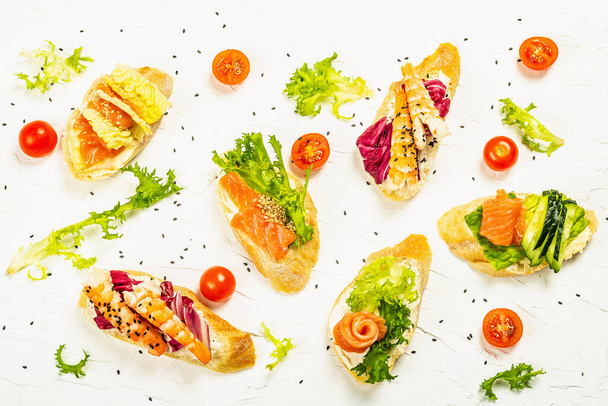 Assorted open sandwiches with salted salmon, boiled shrimps, cream cheese, salad leaves and cherry tomatoes. Seafood, healthy food. White putty background, creative flat lay, top view - Photo, image