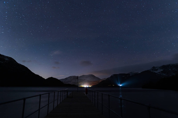 A view of the night sky from Aira Force steamer jetty with the glow of a car lights shinning through the trees. - Fotó, kép