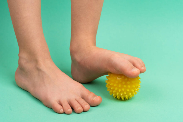 yellow needle ball for massage and physical therapy on a green background with a childs foot, the concept of prevention and treatment of foot valgus - Foto, afbeelding