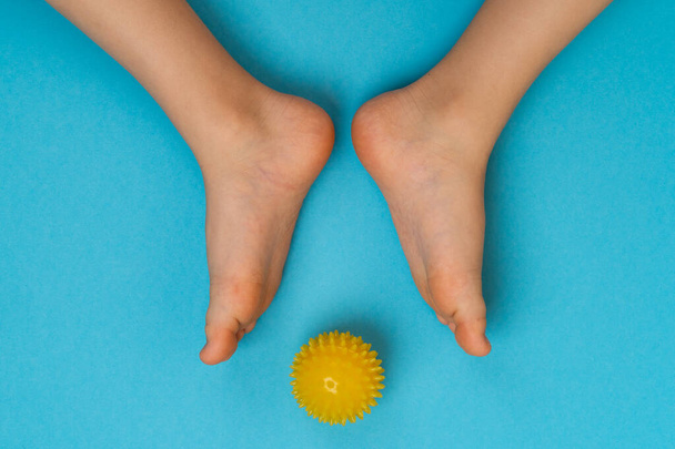 Gelber Nadelball für Massage und Physiotherapie auf blauem Hintergrund mit dem Bild der Kinderfüße, dem Konzept der Vorbeugung und Behandlung von Hallux valgus - Foto, Bild