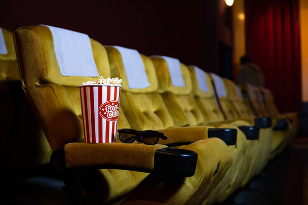 Popcorn and 3d glasses on yellow armchair in cinema with copy space. - Fotoğraf, Görsel