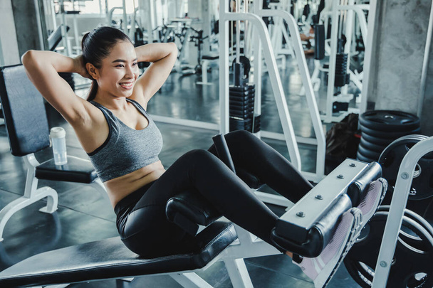 Сексуальная девушка выполняет сидеть упражнения, чтобы укрепить свои основные мышцы живота. Молодая женщина делает приседания на скамейке в современном спортзале. - Фото, изображение