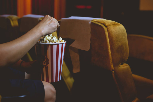 Close-up hand plukken popcorn uit de popcorn emmer die wordt uitgevoerd tijdens het kijken naar een film in een bioscoop. - Foto, afbeelding