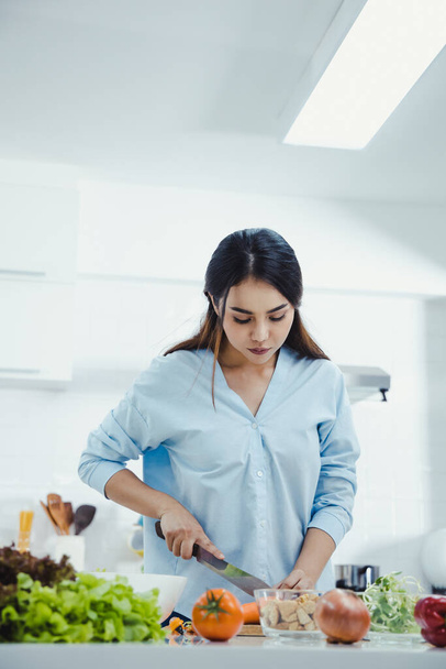 Pystysuora laukaus onnellinen nuori nainen tekee terveellistä salaattia keittiössä kotona hymyillen. Kotona on terveellistä ruokaa. Terveellisen elämäntavan käsite. Nainen tekee tuoretta salaattia keittiössä. - Valokuva, kuva