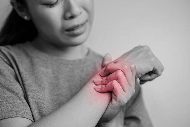 Woman suffering from pain in wrist. Pain in a women wrist. Young woman holding her painful wrist on wall background. - Photo, Image
