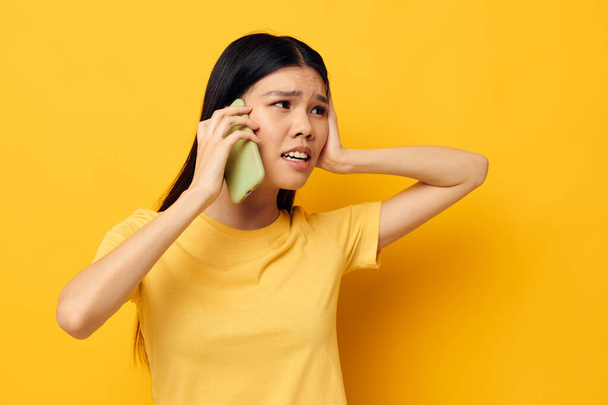 Charming young Asian woman communicates on the phone emotions yellow background unaltered - Valokuva, kuva