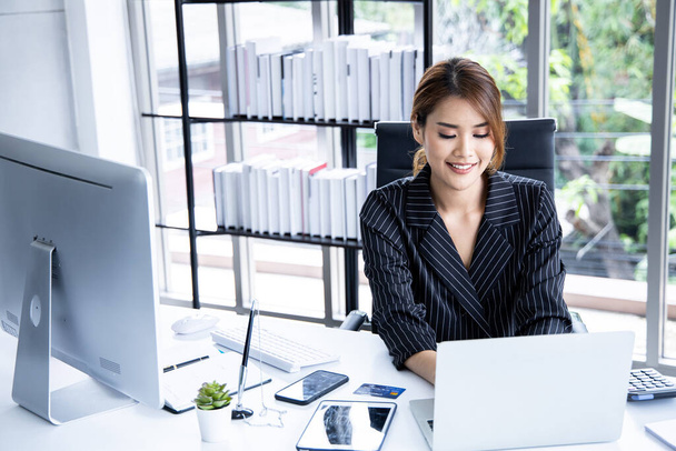 Молодая женщина печатает на ноутбуке с улыбкой, сидя на своем рабочем месте в офисе. Деловая женщина использует ноутбук во время работы в офисе. - Фото, изображение