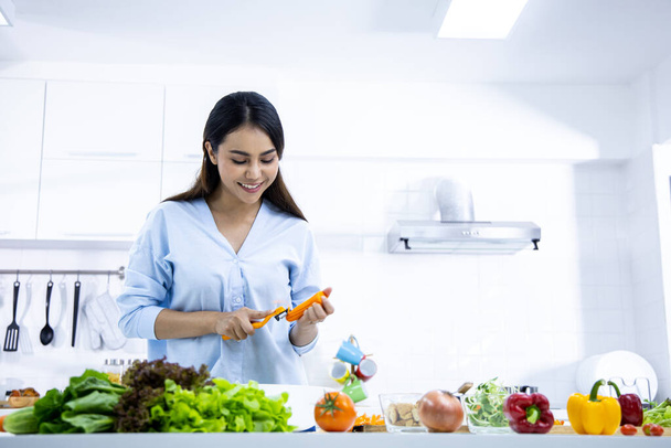 Mujer joven feliz haciendo ensalada saludable en la cocina en casa con una sonrisa. Comida saludable en casa. concepto de estilo de vida saludable. - Foto, Imagen