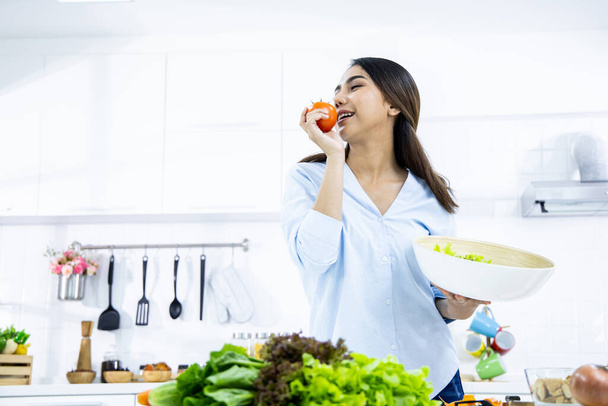 Gelukkige jonge vrouw maakt gezonde salade in de keuken thuis met een glimlach. Gezond eten thuis. Gezond levensstijl concept. - Foto, afbeelding