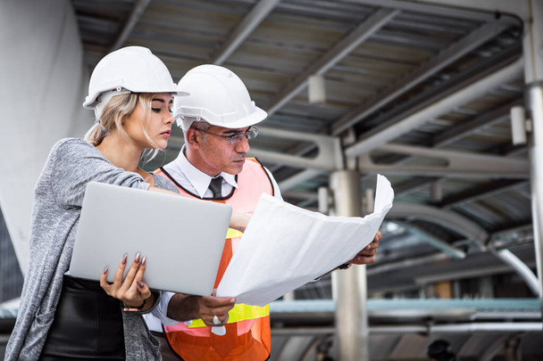 Male and female industrial engineers planning on blueprint and laptop at work site. - Photo, Image