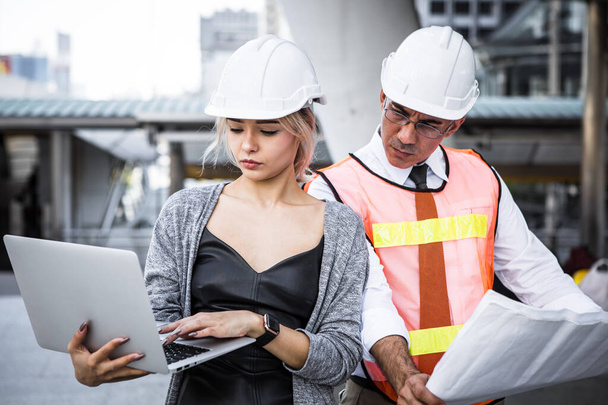 Male and female industrial engineers planning on blueprint and laptop at work site. - Photo, image