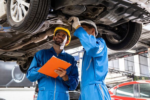 Two mechanic was checking the car suspension. Vehicle raised on lift at maintenance station. Car mechanic working at automotive service center. - Foto, Imagem