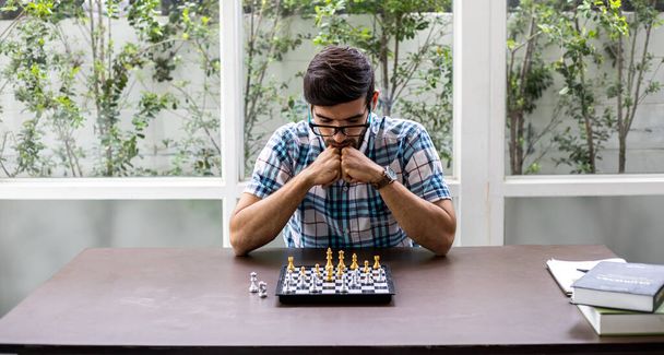 Mann entwickelt Schachstrategie, spielt Brettspiel. Menschlich denkende Schachfigur mit Teamstrategie und Führungskonzept. Umklammerte Hände planen Strategie mit Schachfiguren auf dem Tisch. - Foto, Bild