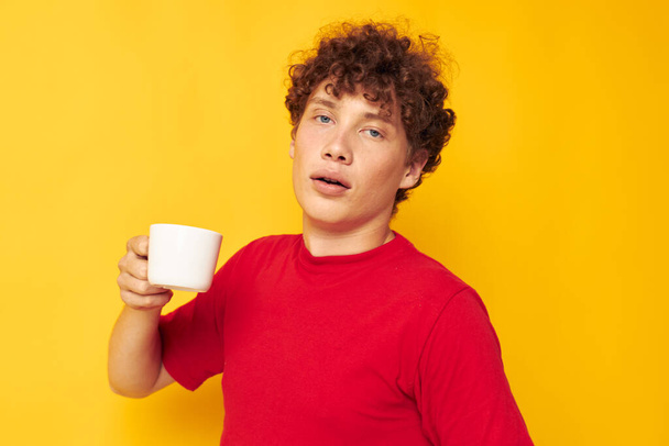 portrait of a young curly man in a red T-shirt with a white cap in his hands isolated background unaltered - Foto, Imagen