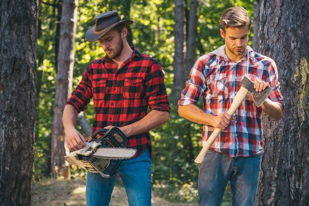 Man with axe in forest. Lumberjack woodcutter in a plaid shirt. Lumberjack brutal bearded man in red checkered shirt. Forest workers. - Photo, Image