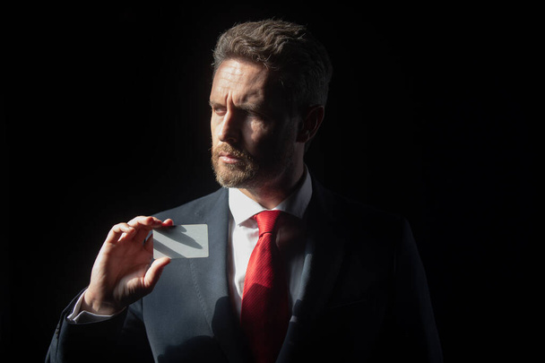 Portrait of businessman with credit card standing on black background, isolated. - Фото, зображення