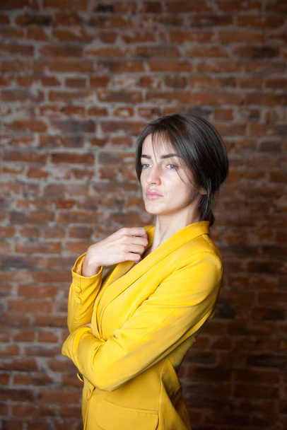 Retrato de hermosa chica en chaqueta amarilla contra la pared de ladrillo rojo.  - Foto, Imagen
