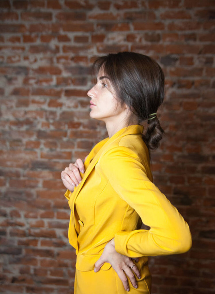 Portrait of   beautiful girl in   yellow jacket against   red brick wall.  - 写真・画像