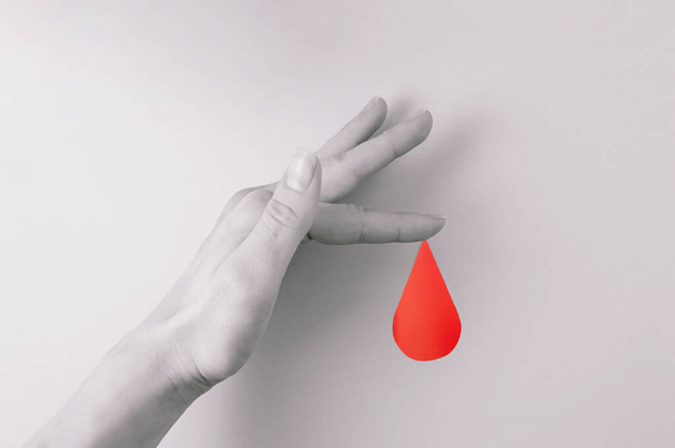 Η μινιμαλιστική έννοια της κόκκινης σταγόνας αίματος που βγαίνει από ένα δάχτυλο. - Φωτογραφία, εικόνα