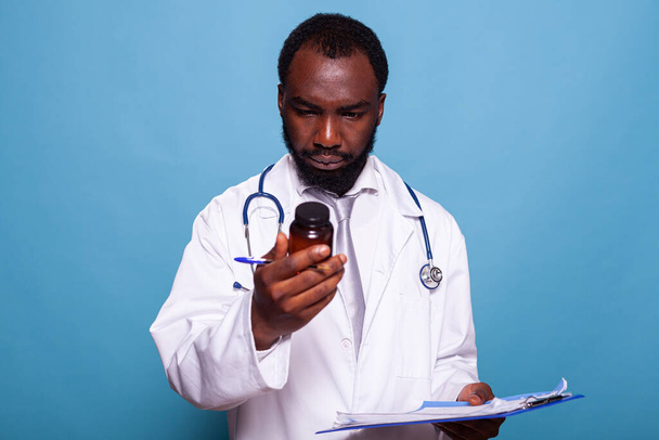 Medico con stetoscopio guardando bottiglia pillola prescrizione mentre tenendo appunti - Foto, immagini