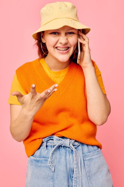 funny girl in an orange sweater in yellow hat talking on the phone pink background unaltered - Photo, image