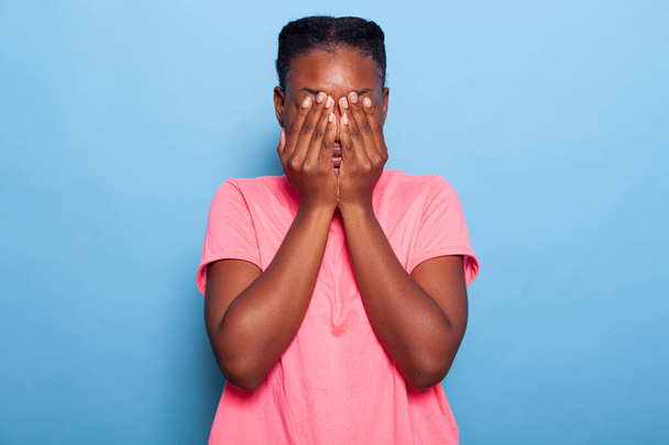 Πορτραίτο τρομοκρατημένης εσωστρεφούς αφροαμερικάνας νεαρής γυναίκας που καλύπτει το πρόσωπο με τα χέρια της - Φωτογραφία, εικόνα