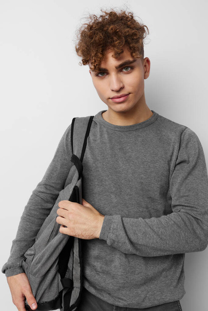 Attractive man in a gray sweater backpack fashion light background - Fotó, kép