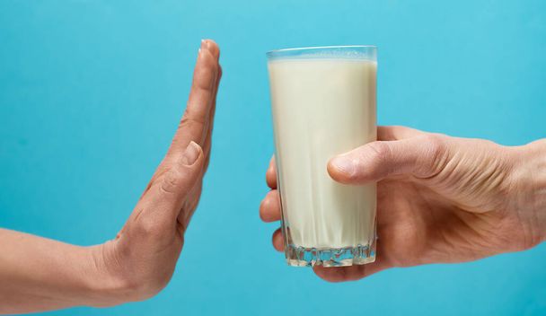 Hand weigeren een glas melk op blauwe achtergrond. Lactose-intolerantie - Foto, afbeelding