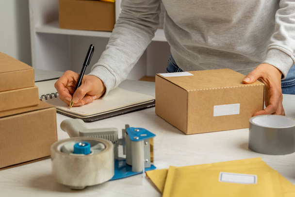 Женщина отправляет посылку в коробке службой доставки и пишет заметки - Фото, изображение