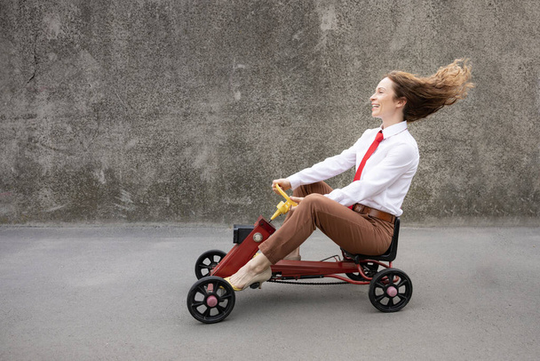 Portrait of funny businesswoman outdoor. Woman driving retro pedal car. Back to work, start up and business idea concept - Zdjęcie, obraz