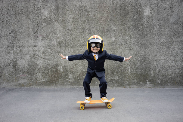 Happy child pretend to be businessman. Funny kid riding skateboard outdoor. Back to work, start up and business idea concept - Photo, image