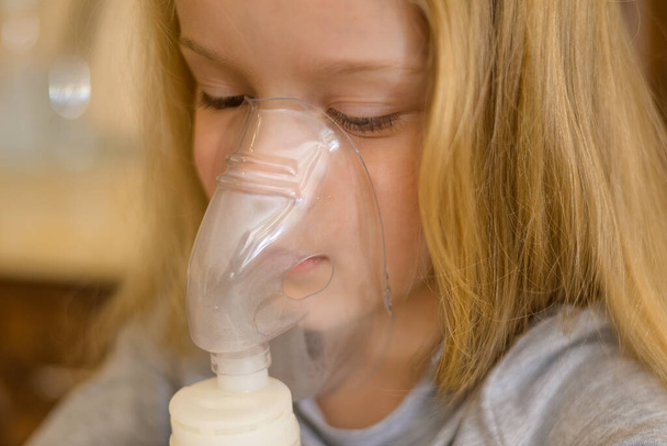 close-up portrait of child at home with nebulizer mask on face, taking inhalation to cure - Valokuva, kuva