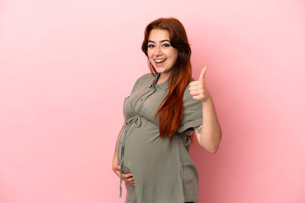 Młoda ruda biała kobieta izolowana na różowym tle w ciąży i z kciukiem w górze - Zdjęcie, obraz