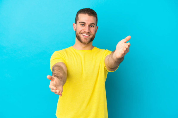 Νεαρός όμορφος καυκάσιος άνδρας απομονωμένος σε μπλε φόντο παρουσιάζοντας και καλώντας τον να έρθει με το χέρι - Φωτογραφία, εικόνα