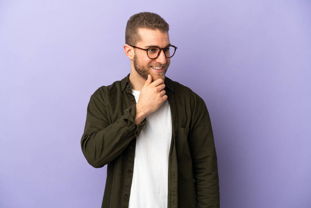 Young handsome caucasian man isolated on purple background looking to the side and smiling - Fotó, kép