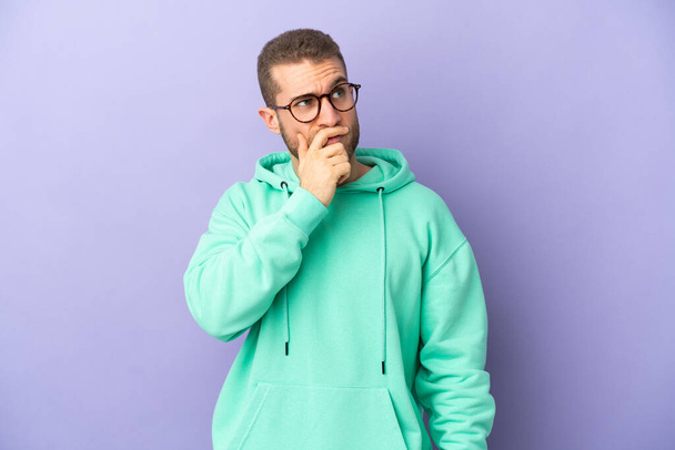 Young handsome caucasian man isolated on purple background having doubts and with confuse face expression - Фото, изображение