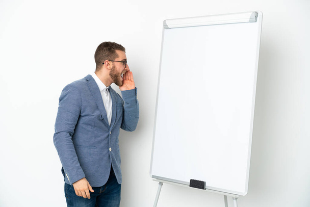 Νεαρή επιχειρηματίας δίνει μια παρουσίαση σε λευκό πίνακα απομονωμένη σε λευκό φόντο φωνάζοντας με το στόμα ορθάνοιχτο στο πλάι - Φωτογραφία, εικόνα