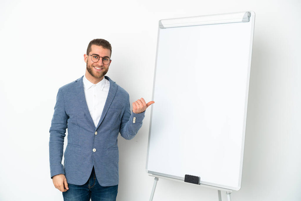 Νεαρή επιχειρηματίας δίνει μια παρουσίαση σε λευκό πίνακα απομονώνονται σε λευκό φόντο δείχνοντας προς τα πλάγια για να παρουσιάσει ένα προϊόν - Φωτογραφία, εικόνα