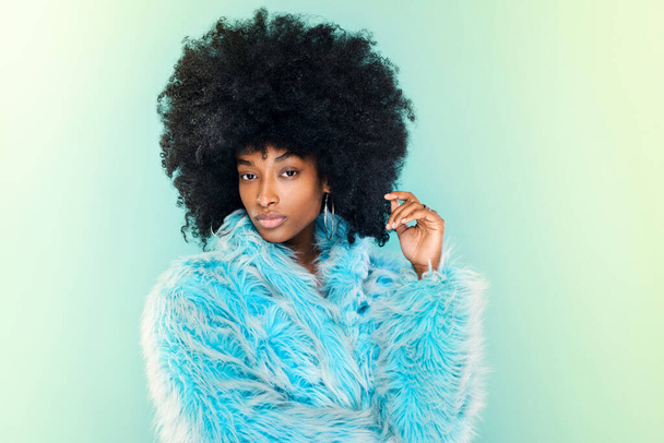 Söpö funky nuori Musta nainen yllään tyylikäs pörröinen viileä sininen talvi alkuun poseeraa yli matching sininen studio tausta - Valokuva, kuva