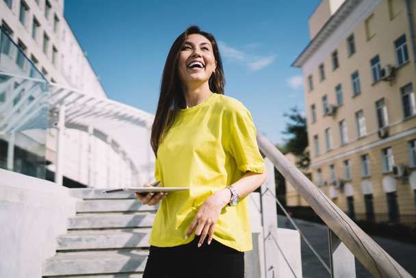 Portrait of cheerful asian female model in casual wear standing on urban setting with touchpad, smiling hipster girl using digital tablet resting on sunny day in town communication in online chat - Fotografie, Obrázek