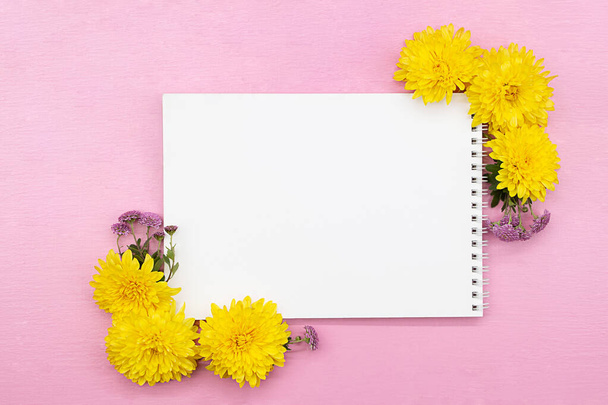 Notepad, space for notes, white sheet with yellow and lilac chrysanthemums, frame of flowers on pink background. Holiday, Spring, Summer, Autumn, Birthday, Mothers, International Women's Day. Copy space - Фото, изображение
