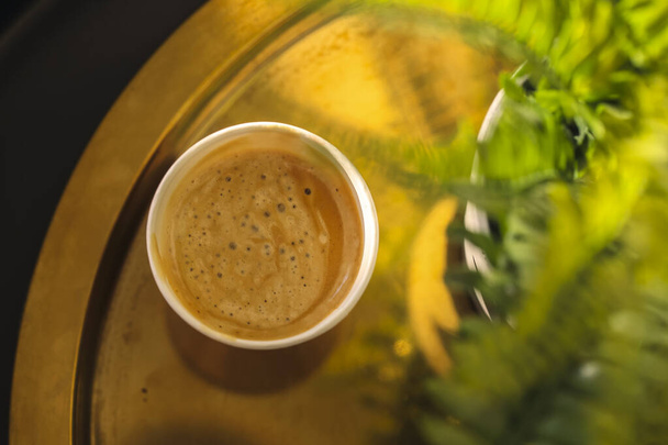 Vista desde arriba de la taza de café en la mesa de café con la planta en maceta verde, enfoque selectivo. Cappuccino aromático fragante recién hecho o latte con espuma servida en coffeeshop - Foto, Imagen