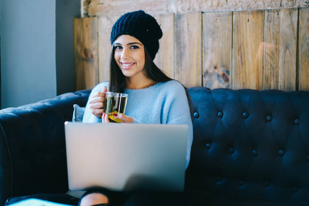 Portrait of happy Caucasian woman with modern netbook smiling at camera while installing media app, cheerful hipster girl 20s with laptop computer posing during break for drinking hot tea - Foto, Imagem