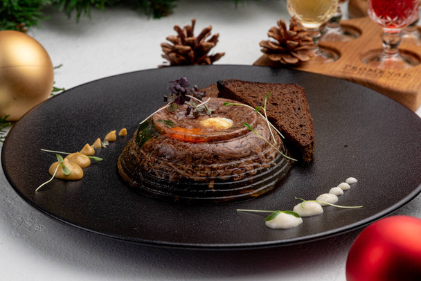 jellied meat served with black bread on a dark plate with mustard and horseradish on a light Christmas background - Foto, imagen