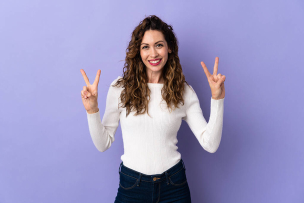 Young caucasian woman isolated on purple background showing victory sign with both hands - Foto, imagen