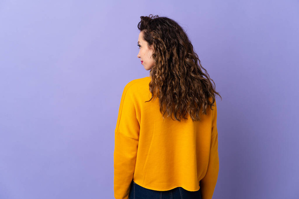 Молода біла жінка ізольована на фіолетовому фоні в положенні спини і дивиться збоку
 - Фото, зображення
